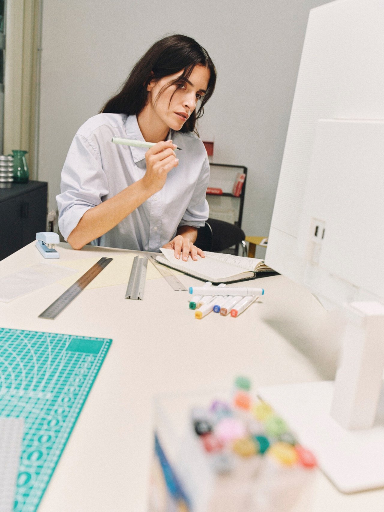 A person making notes beside a computer in a creative workspace.
